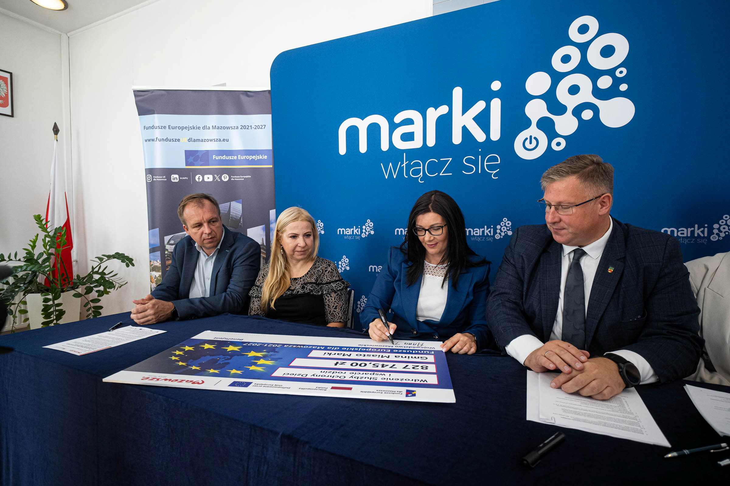 Czlonkini zarzadu A. Brzezinska podpisuje symboliczny czek w towarzystwie wladz Marek